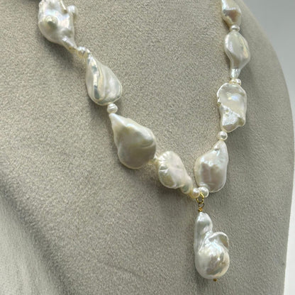 A baroque pearl necklace displayed on a neutral gray mannequin bust. The necklace features irregular, teardrop-shaped white pearls separated by small silver spacer beads and a small gold accent ring near the bottom center, with a larger teardrop pearl hanging as a pendant.