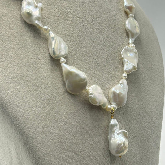 A baroque pearl necklace displayed on a neutral gray mannequin bust. The necklace features irregular, teardrop-shaped white pearls separated by small silver spacer beads and a small gold accent ring near the bottom center, with a larger teardrop pearl hanging as a pendant.