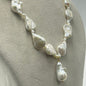 A baroque pearl necklace displayed on a neutral gray mannequin bust. The necklace features irregular, teardrop-shaped white pearls separated by small silver spacer beads and a small gold accent ring near the bottom center, with a larger teardrop pearl hanging as a pendant.